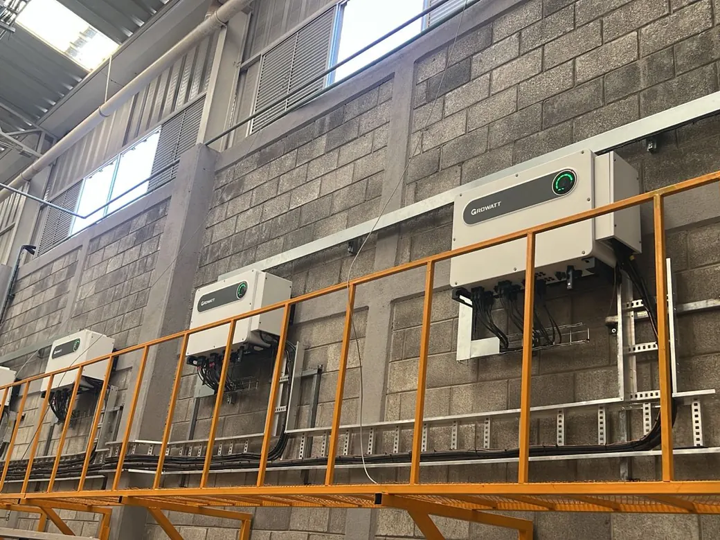 Inversores Growatt encendidos sobre una pasarela de servicio en el muro de la nave de Otates