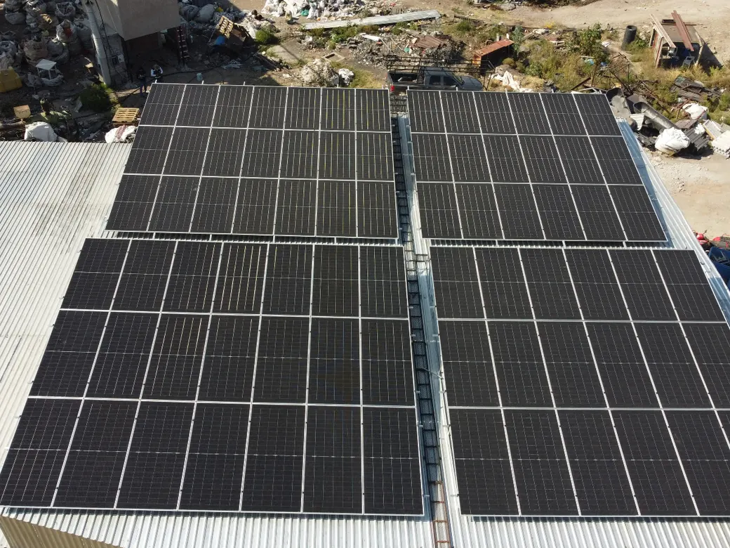Cuatro bloques de módulos solares sobre la lámina, con el patio de materiales al fondo